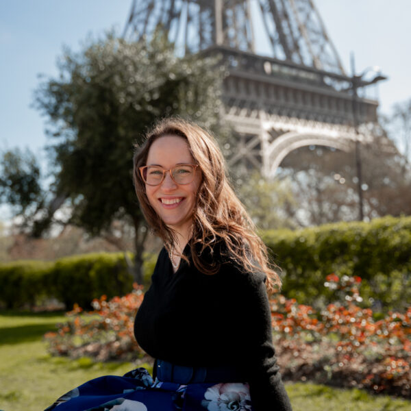 Woman in black sweater smiling and facing camera with the eiffel tower behind her.