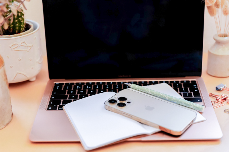 Open pink laptop with open notebook and phone on the keyboard
